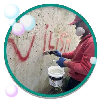 Man utilizes cleaning solution to remove graffiti from wall while wearing protective equipment