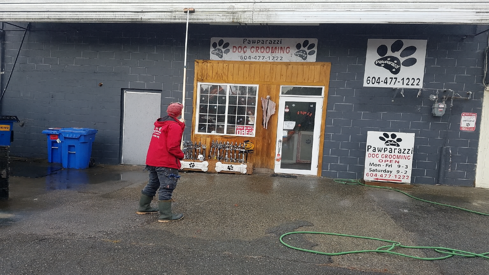 The Environmental Benefits of Brush Washing2 A Maple Washing worker in a red jacket uses a long-handled brush to clean the exterior wall of Pawparazzi Dog Grooming, demonstrating eco-friendly brush washing on a gray brick building.