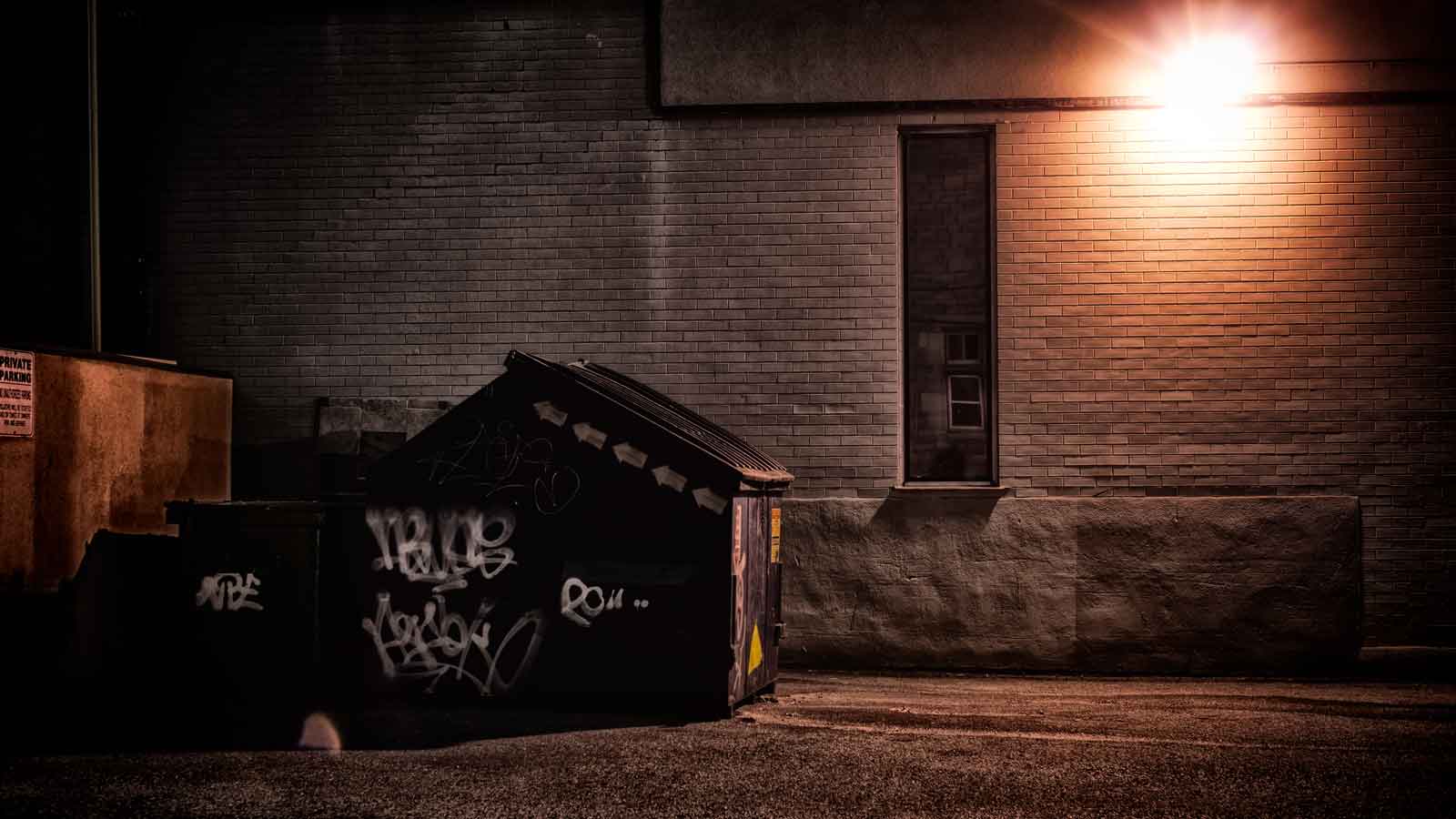 Graffiti Removal in BC A dirty, dark, shadowy and dangerous looking urban back-alley at night time with garbage dumpster.