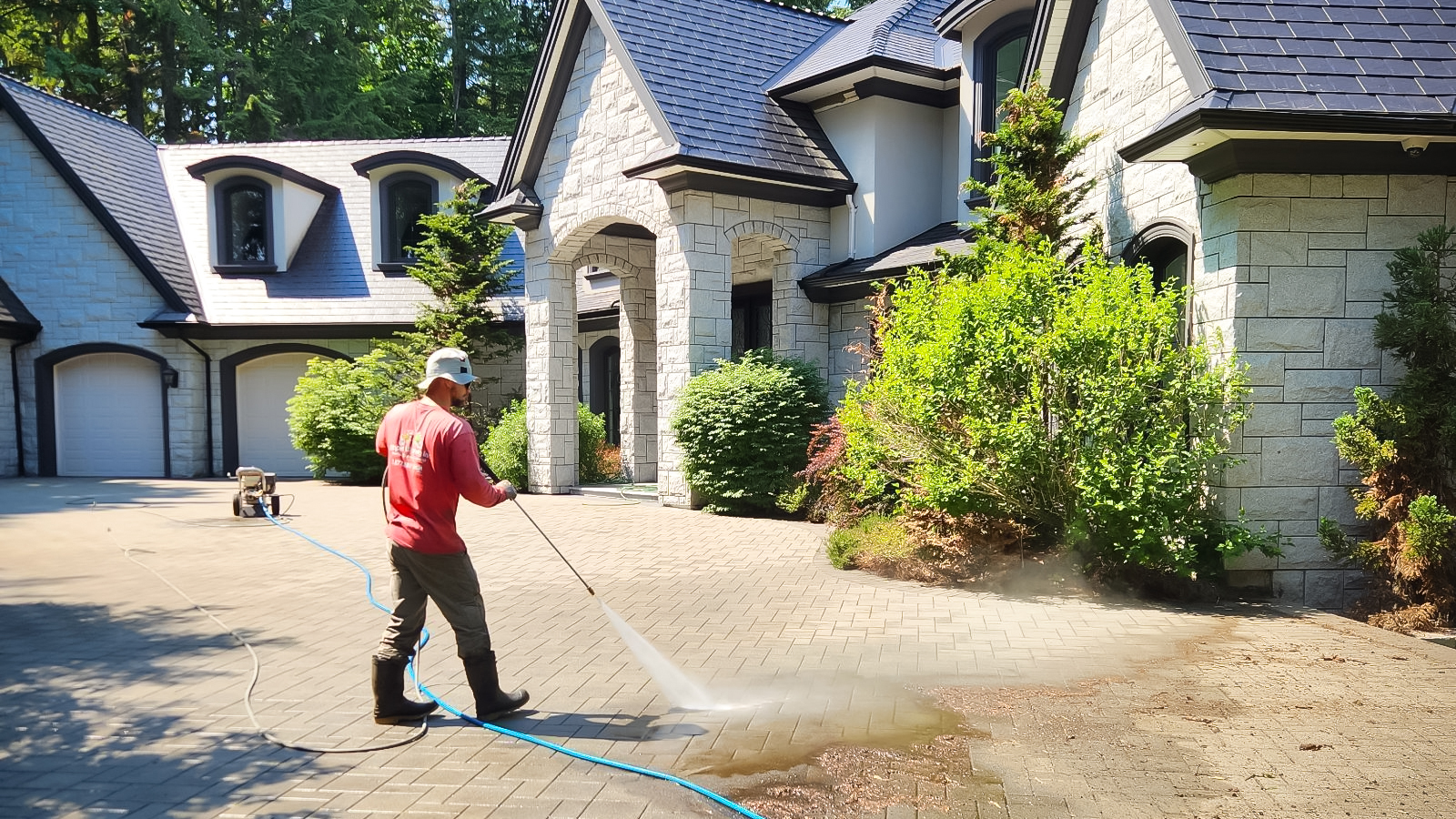 Maple Washing Employee is using a pressure washer on the pavers of a driveway in front of a beautiful home.