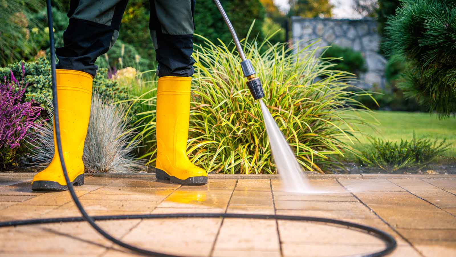 Pressure Washing in Maple Ridge Close up of a person in yellow boots operating a pressure washing on some pavers.