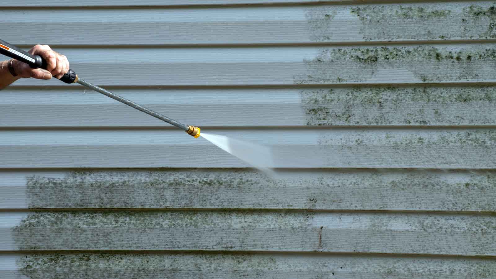 Stage 2 Water Restrictions Close up of a pressure washer removing grime from the siding of a house.